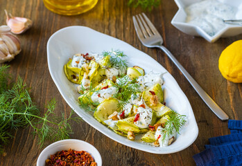 Healthy food, grilled zucchini salad with yogurt sauce, herbs, walnuts in a gray oval plate on a wooden background. Turkish cuisine.