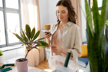 people, gardening and housework concept - happy woman with smartphone and pot flower at home
