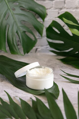 White jar and monstera leaves on marble table close up. Brand packaging mockup