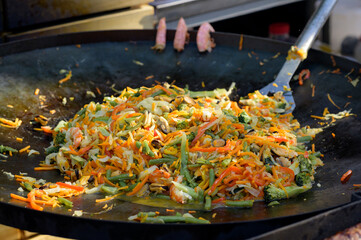 Stir fry noodles with vegetables and shrimps in black iron pan. Slate background. Close up.