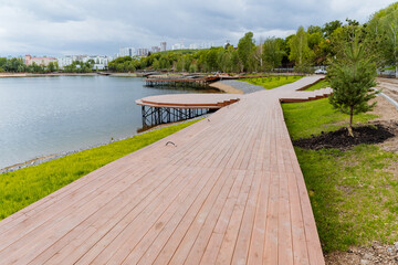 A wooden road along the embankment of the lake, the construction of a city park on a pond, a deck of boards, modern landscape design, landscaping of the city, a place to relax by the water.