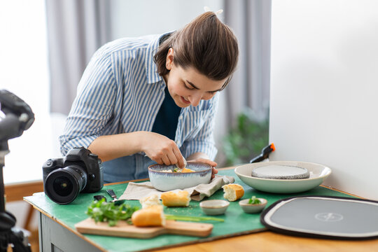 blogging, photographing and people concept - happy smiling female food photographer with camera arranging composition in kitchen at home