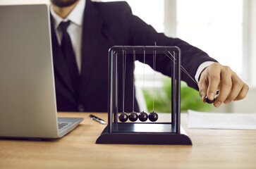 Close up of business leader playing with Newton's cradle on office desk with notebook PC. Man moves...