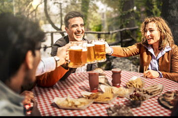Group of cheerful friends toasting beer glasses - Happy people partying and eating in farmhouse...