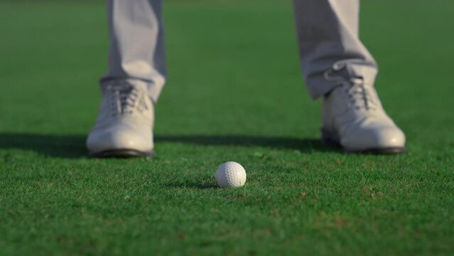 Man legs swinging golf putter club on course field. Player feet stand on grass.