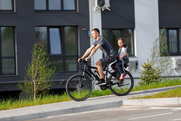 Fototapeta premium The father rides on a bicycle small daughter in a children's seat