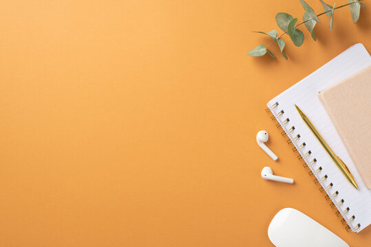 Business concept. Top view photo of workplace white computer mouse wireless earbuds organizers gold pen and eucalyptus branch on isolated orange background with copyspace