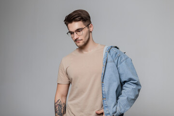 Fashionable handsome stylish man model hipster with hair and vintage glasses with a fashion denim...