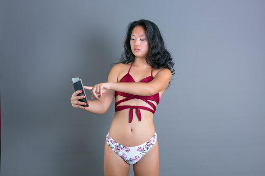 Young Chinese girl in bikini looking at smarfone with surprised expression