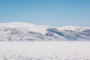 Landscape view of Frozen Cildir lake in Kars and snowy mountains with a blue sky in winter