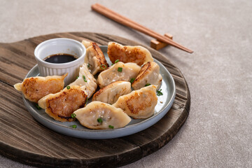 Pan-fried gyoza dumpling jiaozi in a plate with soy sauce on gray table background.