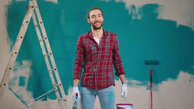 Professional painting man good looking posing in front of the camera holding wall brush roller while have a break he looking straight to the camera