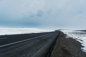Diagonal view of an emtpy asphalt and bending road with lanes and snow in winter