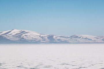 Landscape view of Frozen Cildir lake in Kars and snowy mountains with a blue sky in winter