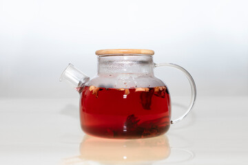 Tea with red berries in a modern glass teapot with reflection and shadows on a gray background