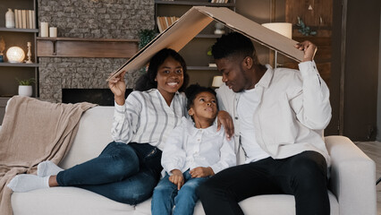African american family parents with daughter little girl adopted child sit on sofa under cardboard roof dreaming about own house relocation home insurance real estate buying flat kid protection