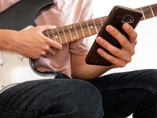 Young man learning to play the electric guitar through an app on his smartphone.