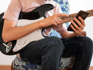 Young man learning to play the electric guitar through an app on his smartphone.
