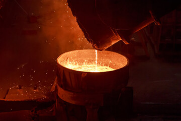 Hot steel pouring from big casting ladle into a mold in an iron foundry.
