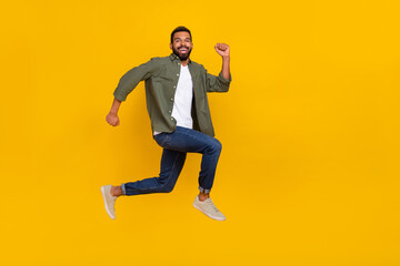 Fototapeta na wymiar Full length photo of funky excited guy dressed green shirt jumping high running fast empty space isolated yellow color background
