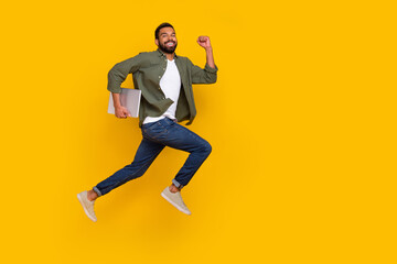 Fototapeta na wymiar Full length photo of cute funky guy dressed green shirt jumping running modern gadget empty space isolated yellow color background