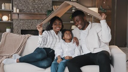 African american family parents with daughter little girl adopted child sit on sofa under cardboard roof dreaming about own house relocation home insurance real estate buying flat kid protection