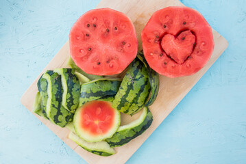 Vitamins for healthy lifestyle in heart shape cut. Two halves of peeled watermelon, fresh from farmers market, ready to eat with someone you love. Tropical summer refreshment on aqua blue background. 