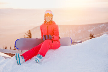 Smile Woman snowboarder in red clothes sitting on snow background sunset forest. Concept banner...