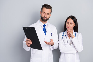 Portrait of two attractive focused skilled smart doctors reading analyzing disease history isolated over grey color pastel background