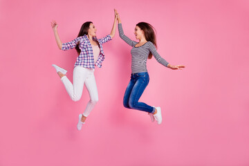 Full length portrait of two excited active people jumping hand give high five isolated on pink...