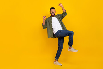Fototapeta na wymiar Full length photo of cheerful lucky guy dressed green shirt rising fists walking empty space isolated yellow color background