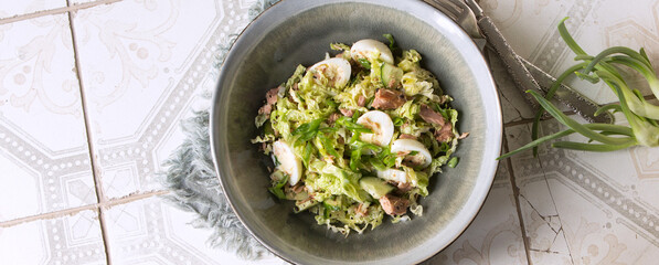 a bowl of salad with Chinese cabbage, tuna and quail eggs on a light table