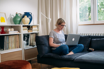 woman using laptop computer sits on sofa in living room