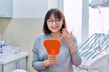 Happy woman dentist patient with mirror in hands looking at her teeth