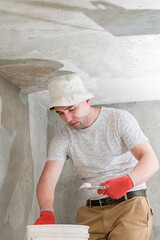 A man with a small spatula applies lime plaster on a large spatula, lime plaster on the walls and ceiling.