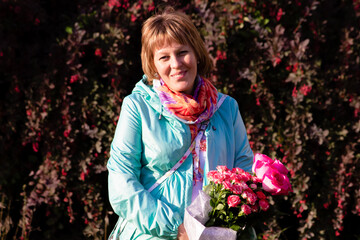 A middle-aged woman with flowers stands on the street and smiles at the camera