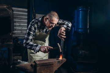 The blacksmith manually forging the red-hot metal on the anvil in smithy.