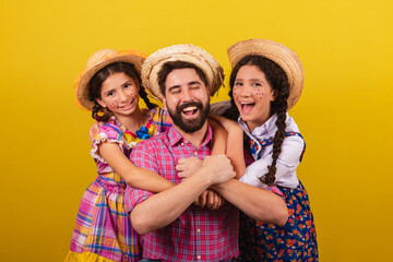 Father and daughters wearing typical clothes for the Festa Junina. Hugging, happy and smiling. For...