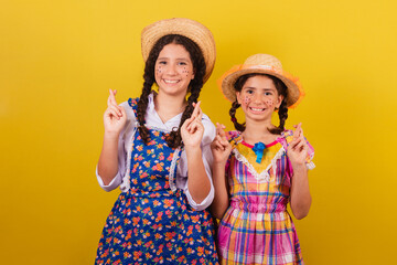 sisters and friends, wearing typical clothes of the Festa Junina. Fingers crossed, twisting,...