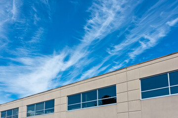 Top of the office building with windows on blue and cloudy sky background