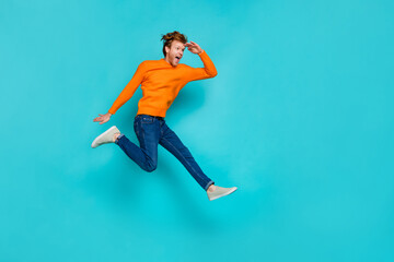 Fototapeta na wymiar Full length photo of impressed excited guy dressed sweater jumping looking far away empty space isolated turquoise color background