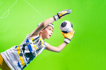 child plays football by being the goalkeeper and saves the ball in a funny way on the green background of the soccer field