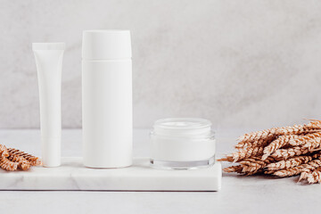 White blank cosmetic bottles and wheat decor for mock up on white marble tray