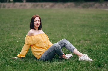 A contented young girl with a square sits in nature on green grass in full growth.