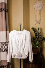 Handmade white silk blouse hanging on a hanger in the room