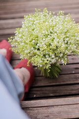 a bouquet of lilies of the valley at the feet of a girl in brown shoes