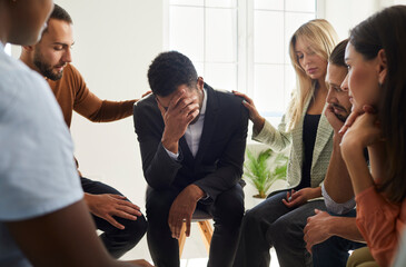 Supportive friends comfort cheer unhappy male colleague feel depressed talk at counseling session....