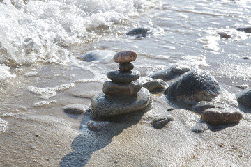 Balance zen stones pyramid on sand beach with splashing waves. Stability, balance, and harmony concept.	