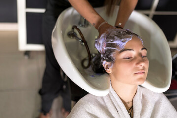 Professional hairdresser washing hair of a beautiful young woman in hair salon.