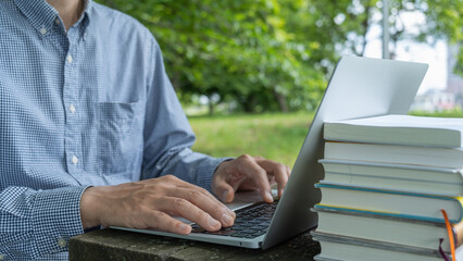 屋外のテーブルでパソコン操作。積まれた本。